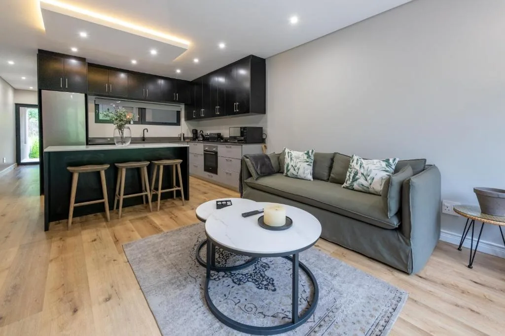 Modern lounge with gray sofa, round white table, and open-plan kitchen area
