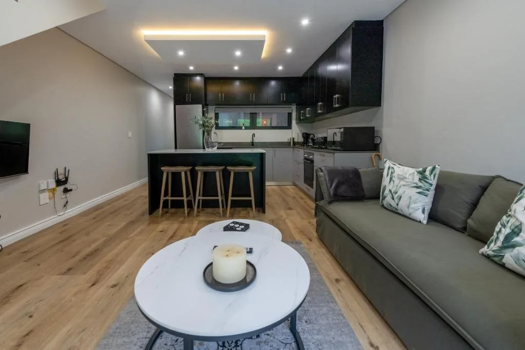 Modern lounge with grey sofa, round marble table, open-plan kitchen with black cabinetry