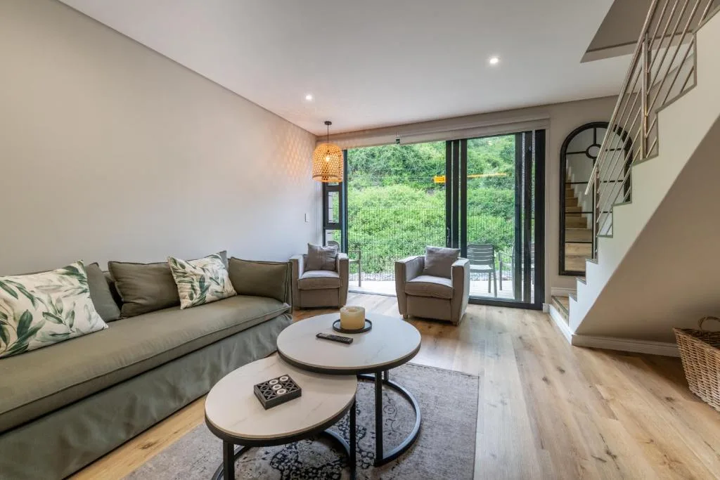 Modern living room with sofa, armchairs, and large glass doors opening to deck