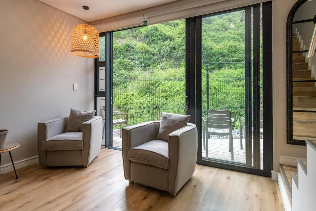 Modern lounge with armchairs, pendant lamp, and forest views through glass doors