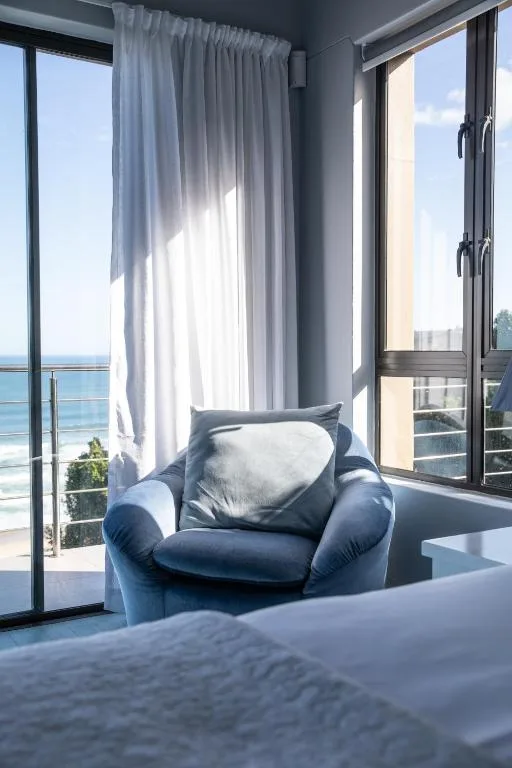 Bright bedroom with blue armchair overlooking ocean views through glass doors
