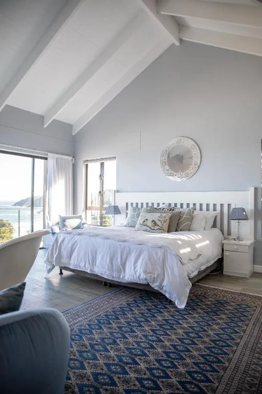 Bright bedroom with white beams, blue bedding, coastal views through windows
