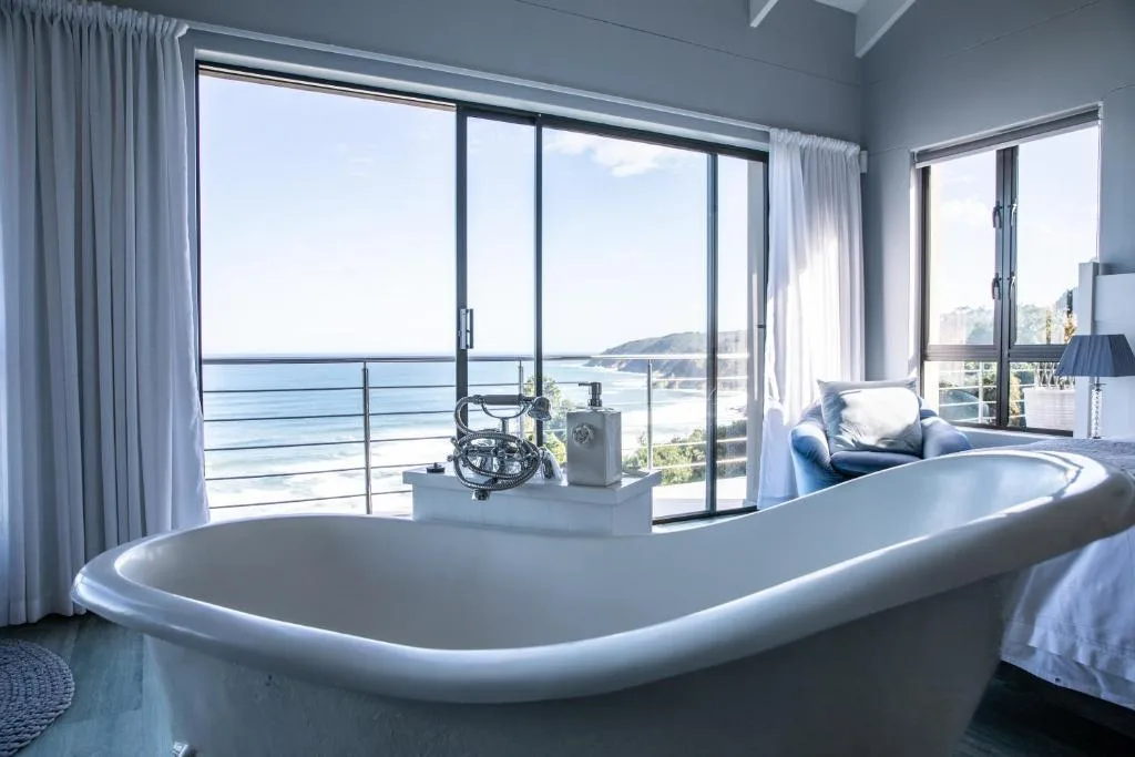 Luxurious bedroom with freestanding bathtub and ocean views through glass doors
