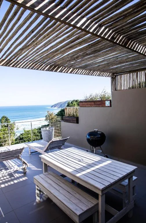Shaded outdoor deck with ocean and beach views, dining table and braai