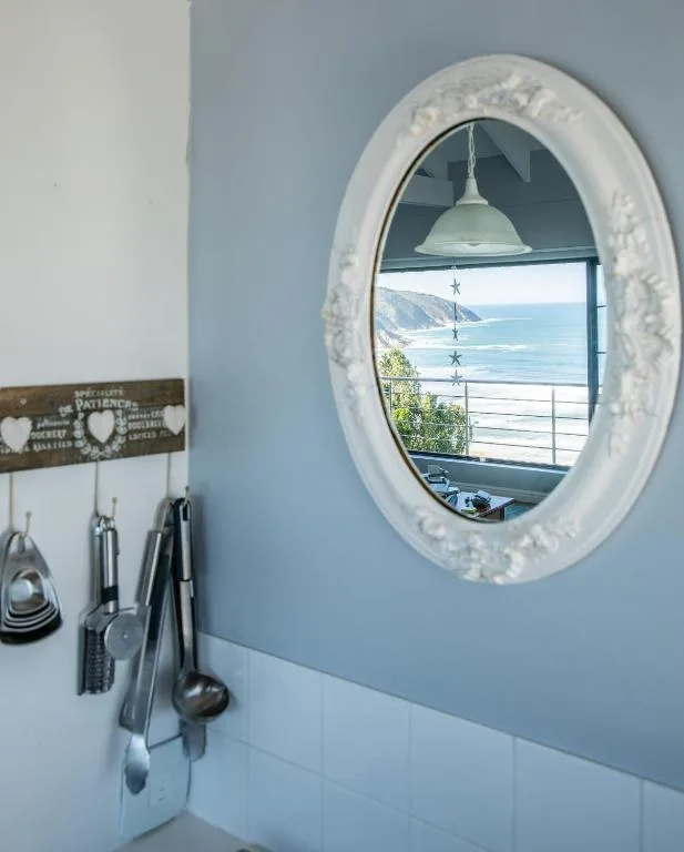 Decorative oval mirror framing coastal ocean view with kitchen utensils below