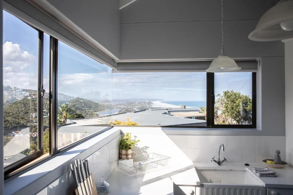 Modern white kitchen with panoramic ocean and mountain views through large windows
