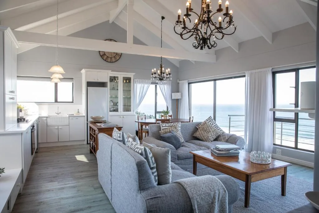 Bright open-plan lounge with gray sofas, chandelier, ocean views through glass doors