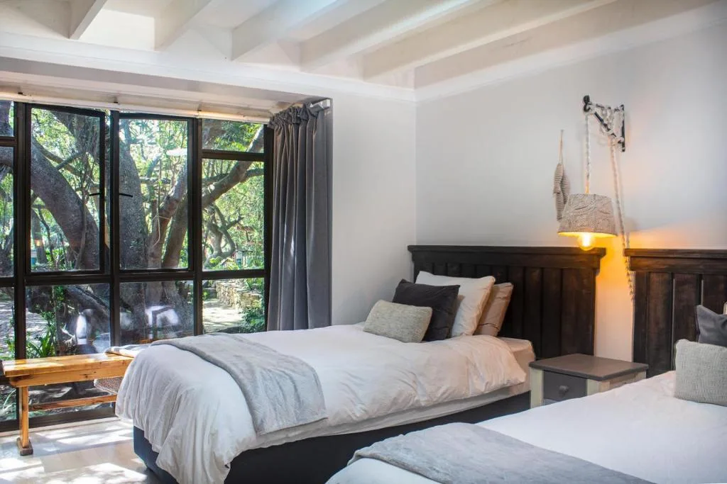 Bright bedroom with two beds, dark headboards, and large windows overlooking trees