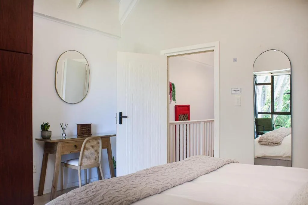 Bright bedroom with bed, desk, mirror, and garden view through glass door