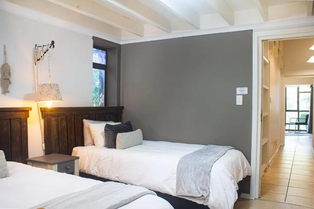 Bright bedroom with two beds, dark headboards, gray accent wall, and wooden beams