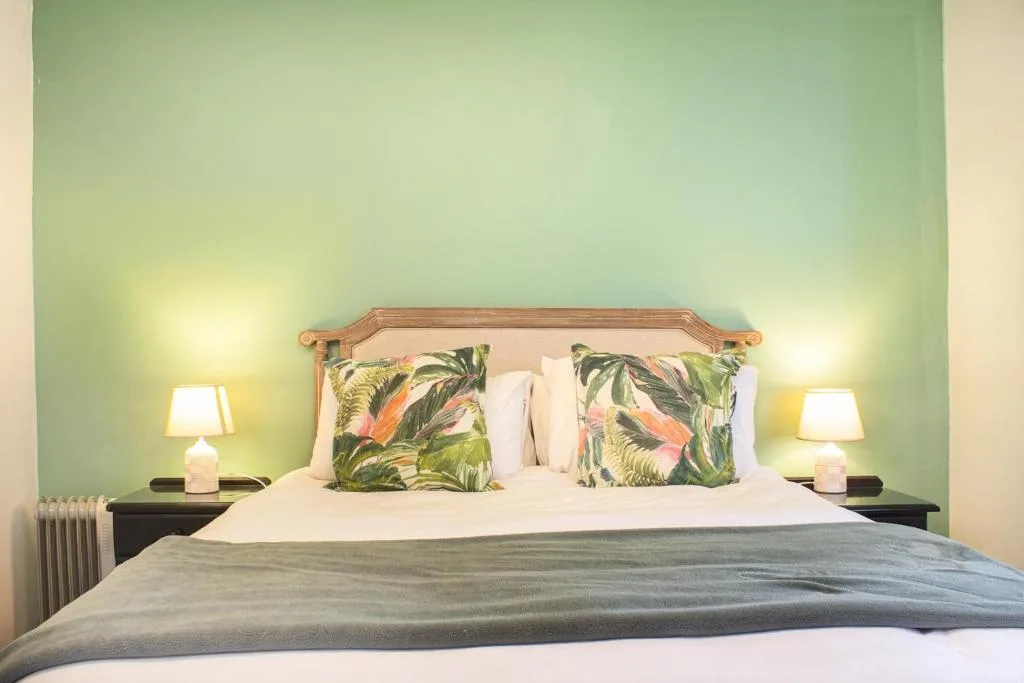 Bright bedroom with green walls, wooden headboard, tropical pillows, and bedside lamps