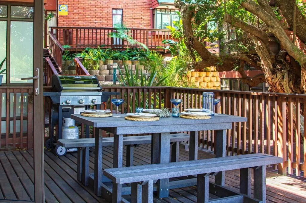 Wooden deck with dining table, bench seating, and built-in braai grill