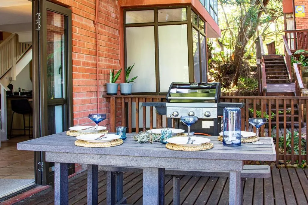 Outdoor dining table with grill and potted plants on wooden deck