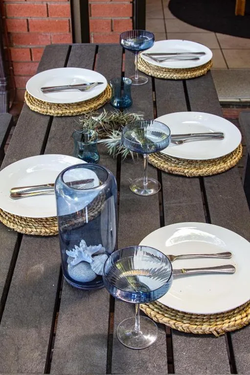 Outdoor dining table with place settings and blue glassware on wooden deck