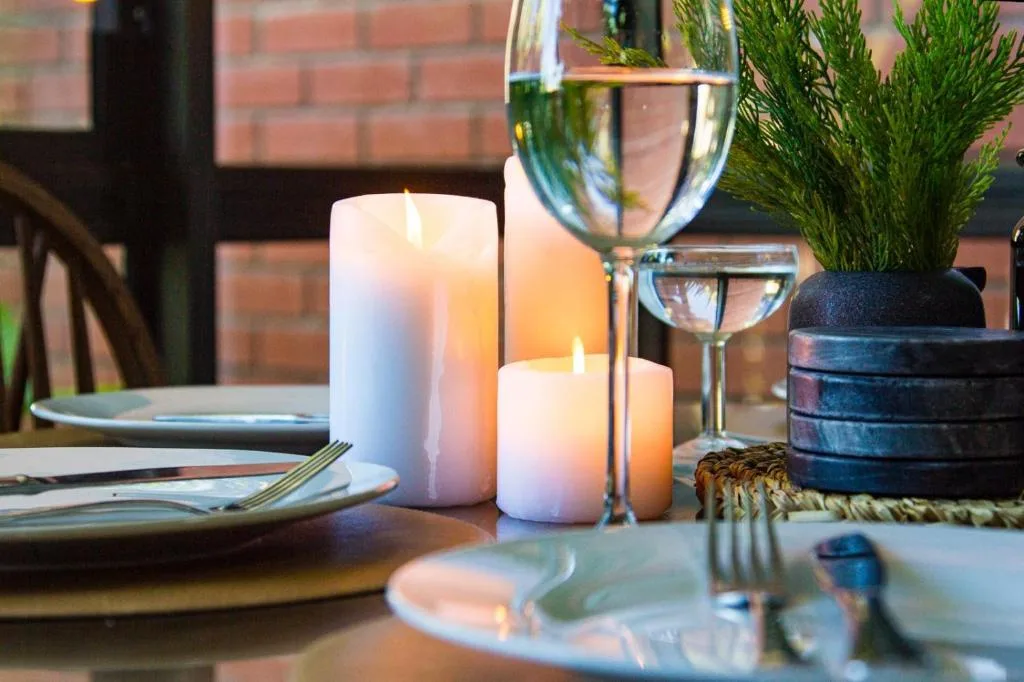 Elegant dining table setting with lit candles, wine glass, and potted plant