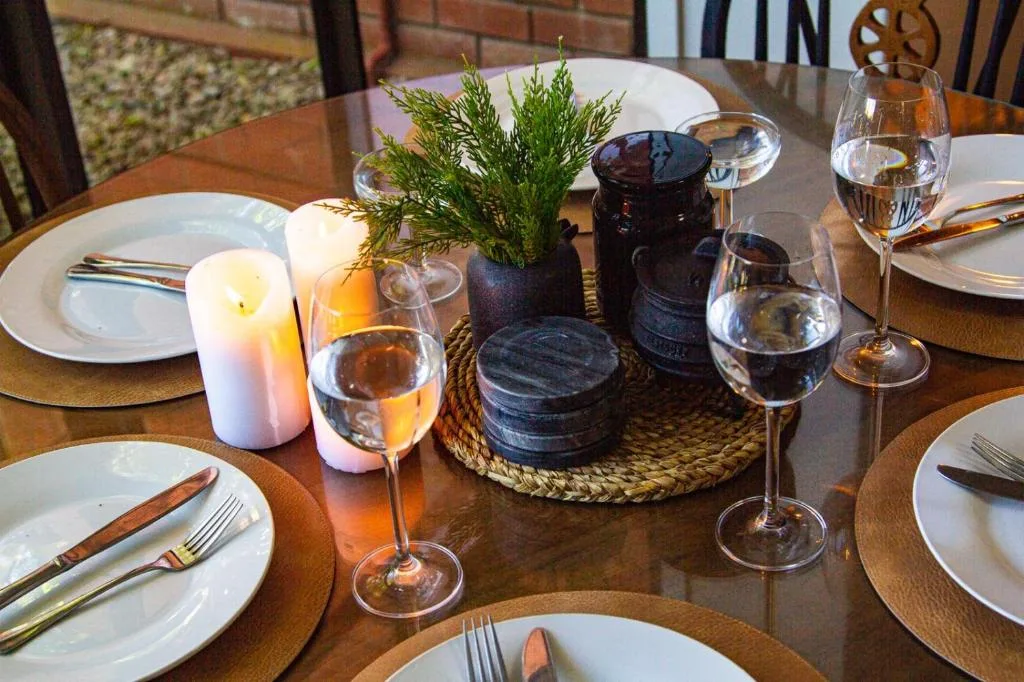 Elegant dining table set with white plates, wine glasses, and greenery centerpiece