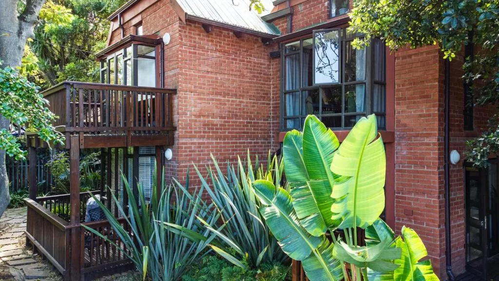 Red brick building facade with wooden deck and lush tropical garden plants