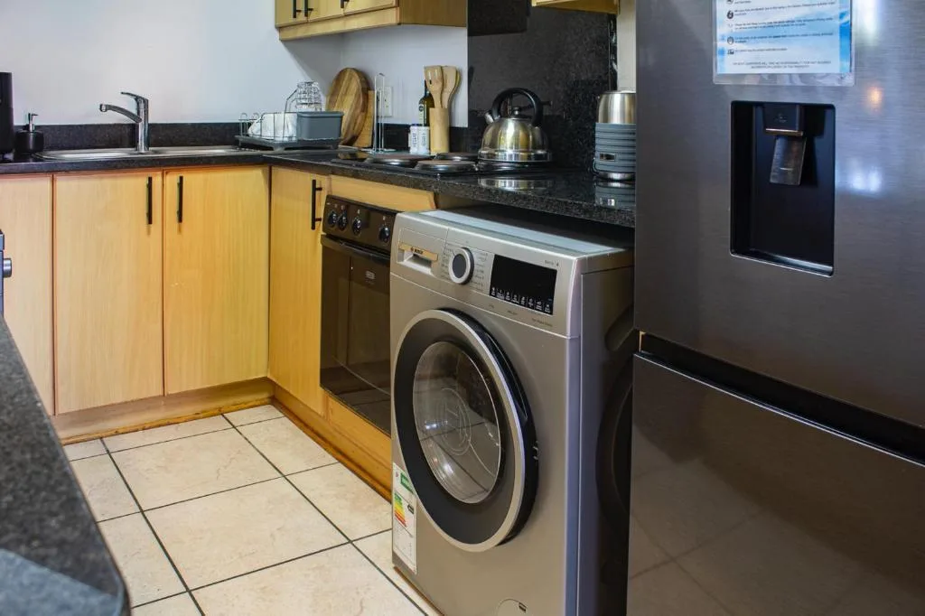 Modern kitchen with wooden cabinetry, black countertop, stainless steel appliances, and washing machine