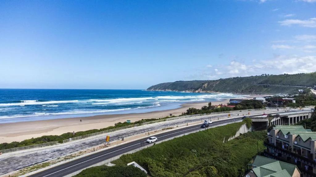 Expansive beach view with golden sand, blue ocean waves, and coastal cliffs
