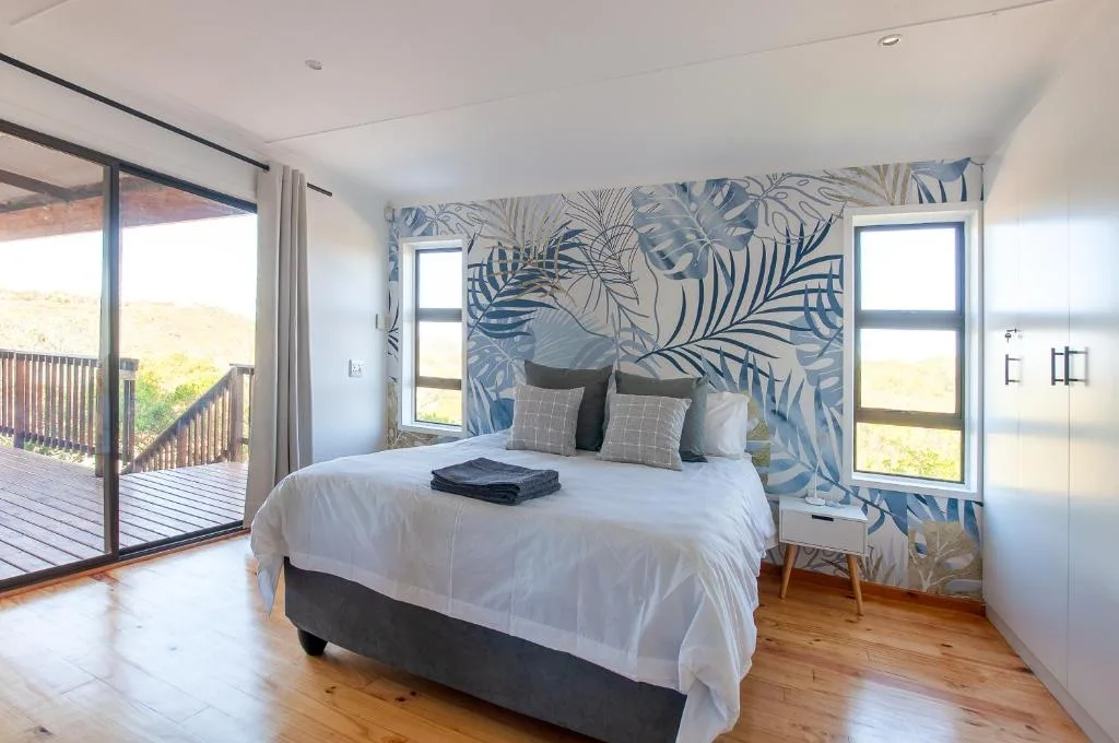 Modern bedroom with queen bed, tropical wallpaper, and deck access overlooking garden.