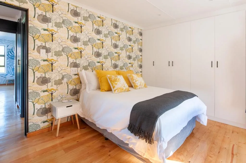 Modern bedroom with patterned feature wall, yellow cushions, white linens