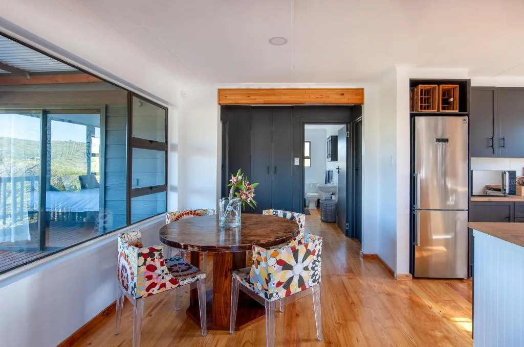 Modern dining area with round wooden table and patterned chairs, open-plan kitchen visible