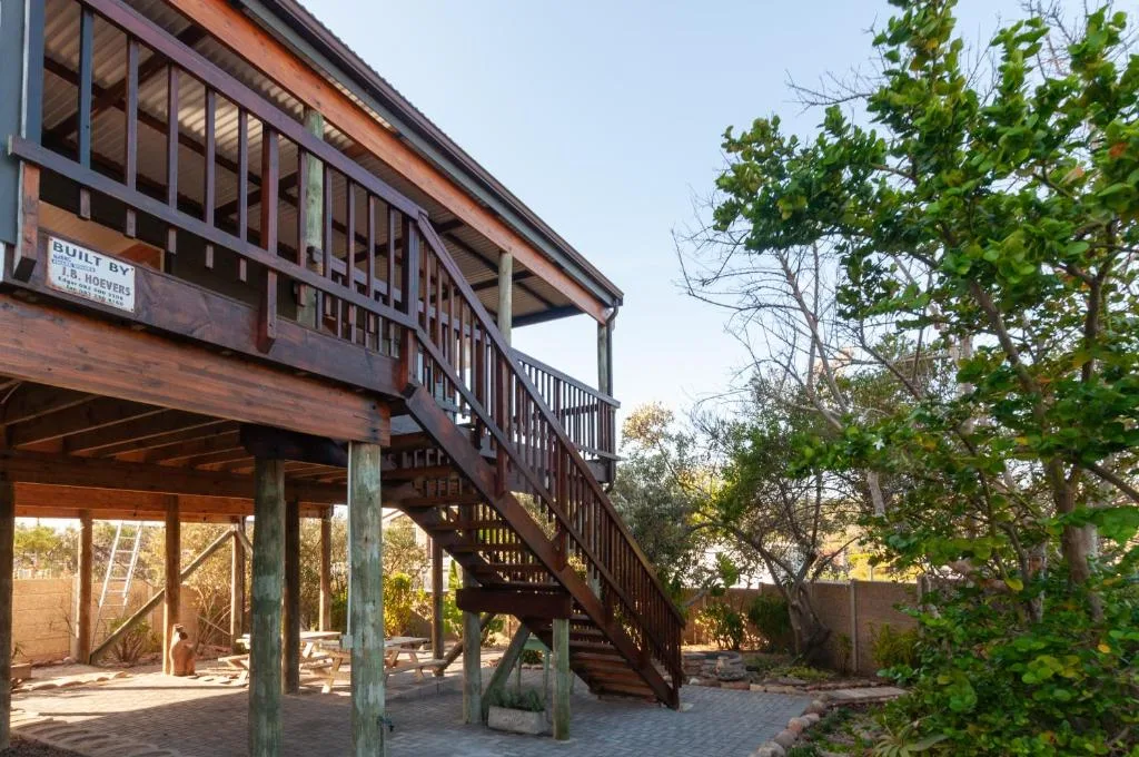 Elevated wooden house with deck and stairs, surrounded by green garden landscape