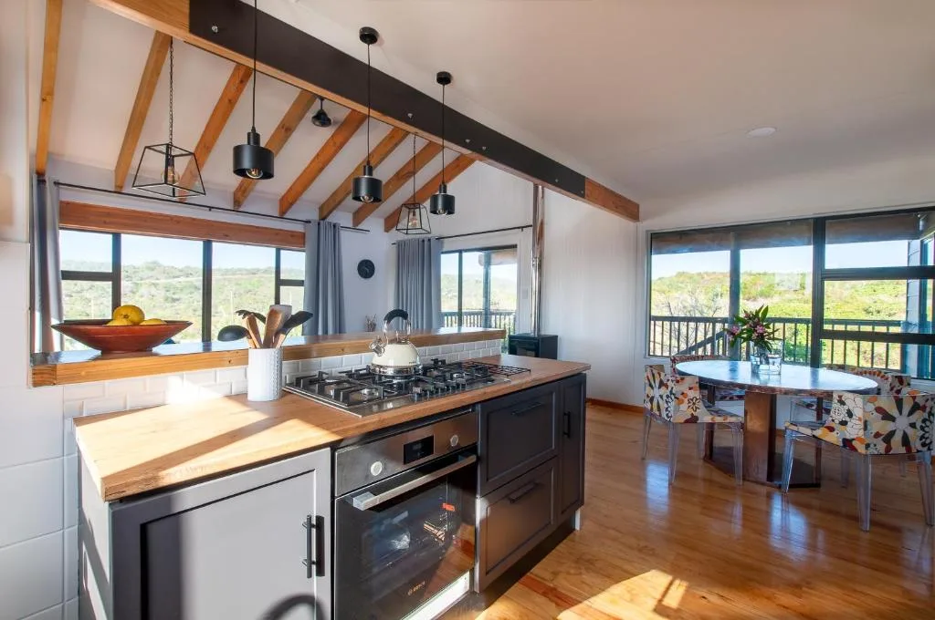 Modern kitchen with gas cooktop, wooden beams, pendant lights, and garden views