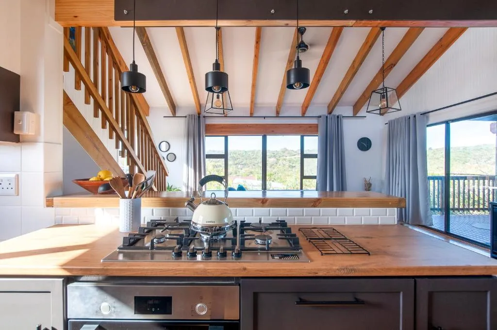 Modern kitchen with gas cooktop, wooden beams, pendant lights, and scenic views