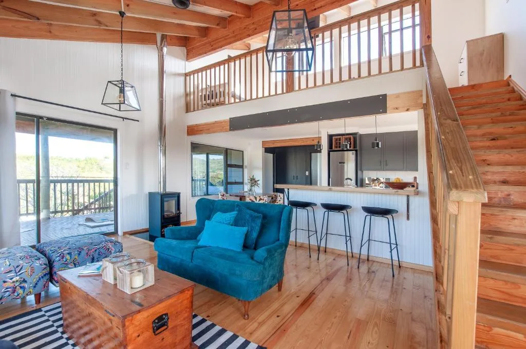 Open-plan lounge with blue sofa, wooden beams, kitchen visible beyond