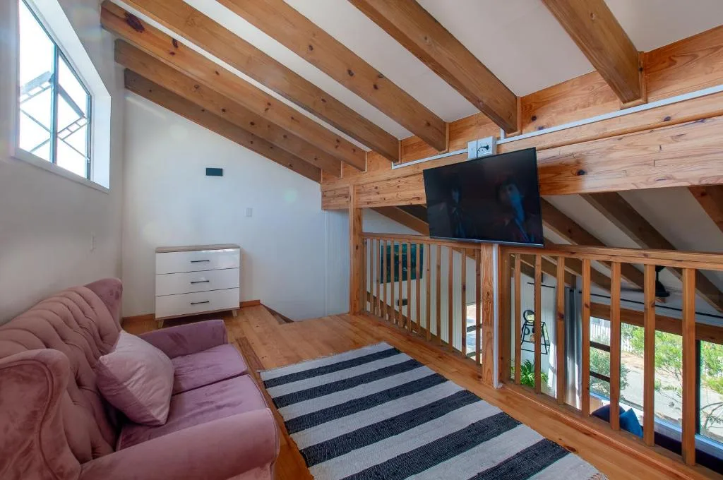 Spacious loft lounge with exposed wooden beams, pink sofa, and wall-mounted television