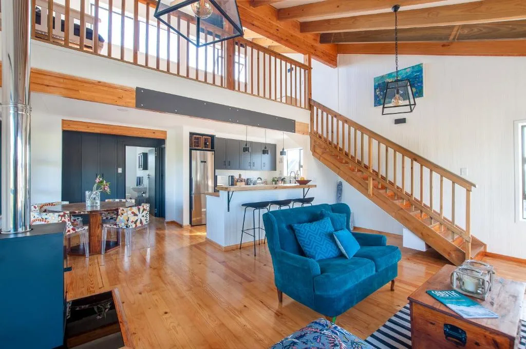Open-plan lounge with blue armchair, wooden beams, and kitchen visible