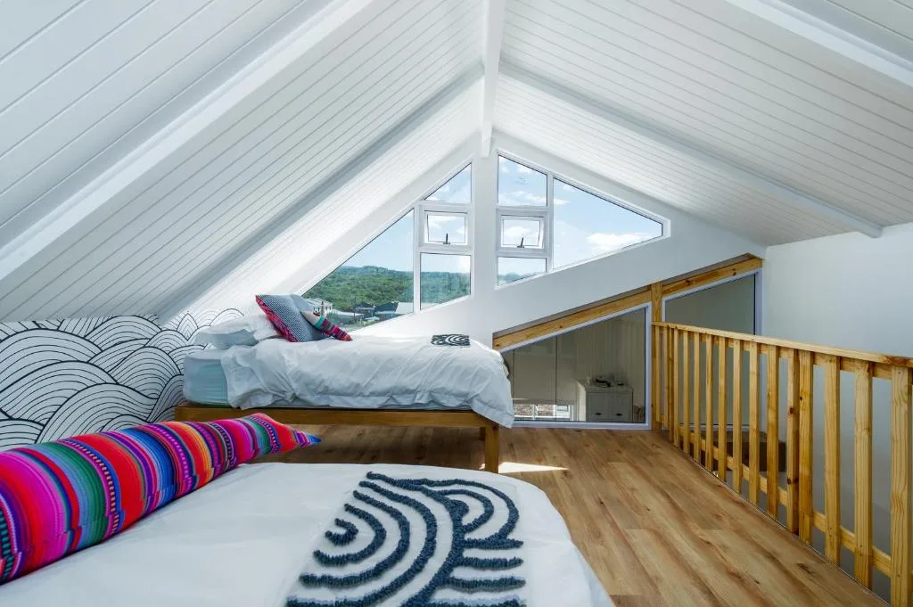Bright attic bedroom with twin beds, colorful pillows, mountain view through skylights