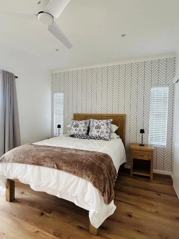 Wooden bed with white linens and brown throw in bright bedroom with geometric wallpaper