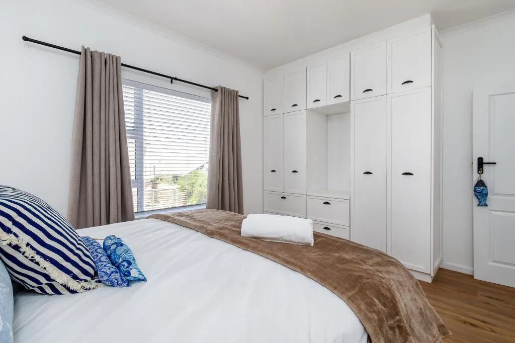Bright bedroom with queen bed, white built-in wardrobes, and garden views