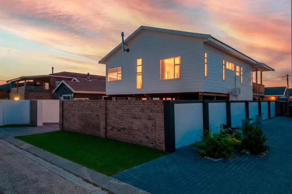 Modern white beach house at dusk with illuminated windows and brick wall