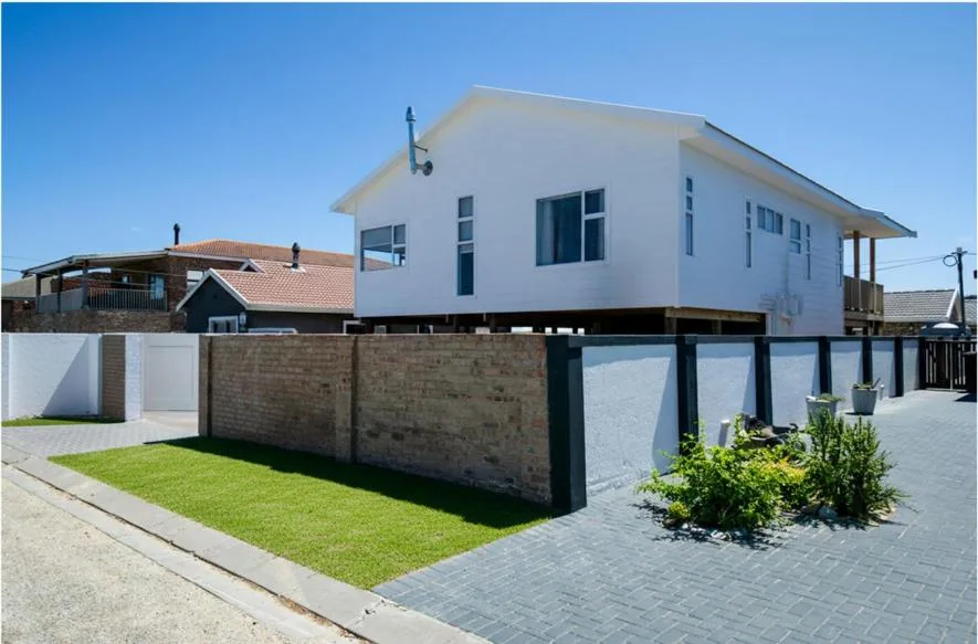 Modern white holiday home elevated on stilts with manicured lawn and driveway