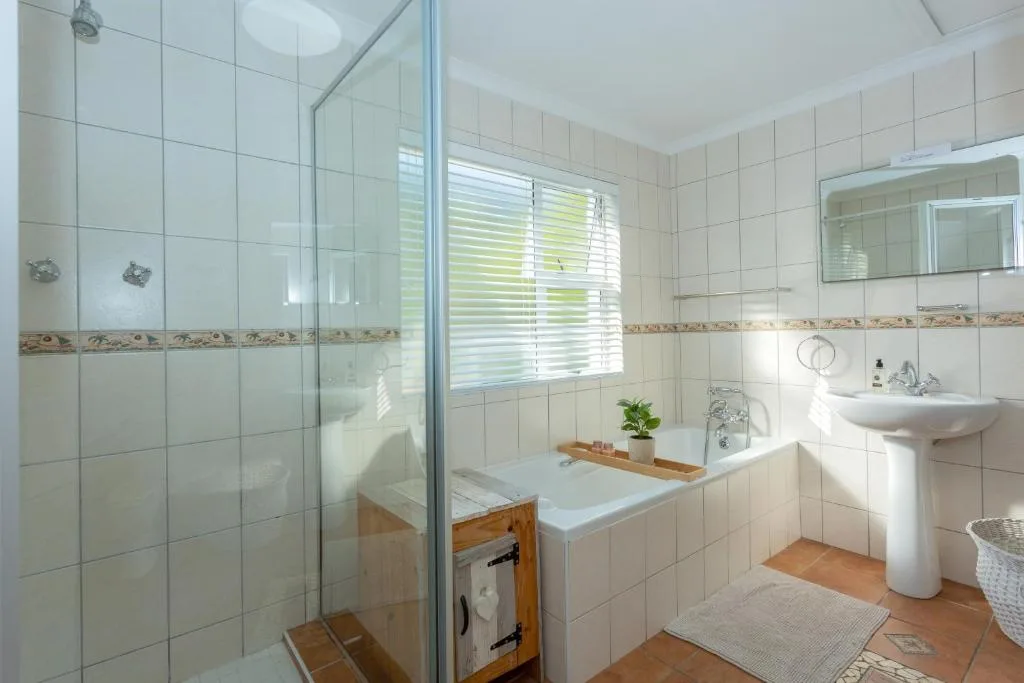 Bright bathroom with glass shower enclosure, white tiles, pedestal sink, and bathtub