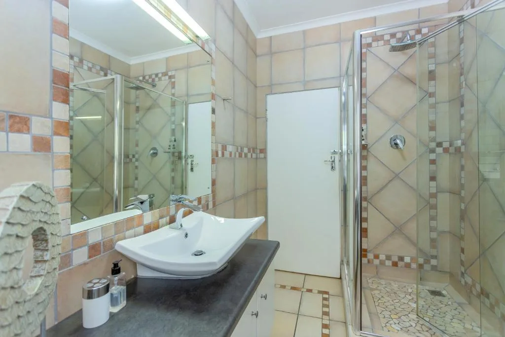 Modern bathroom with curved sink vanity, glass shower enclosure, and terracotta tile work