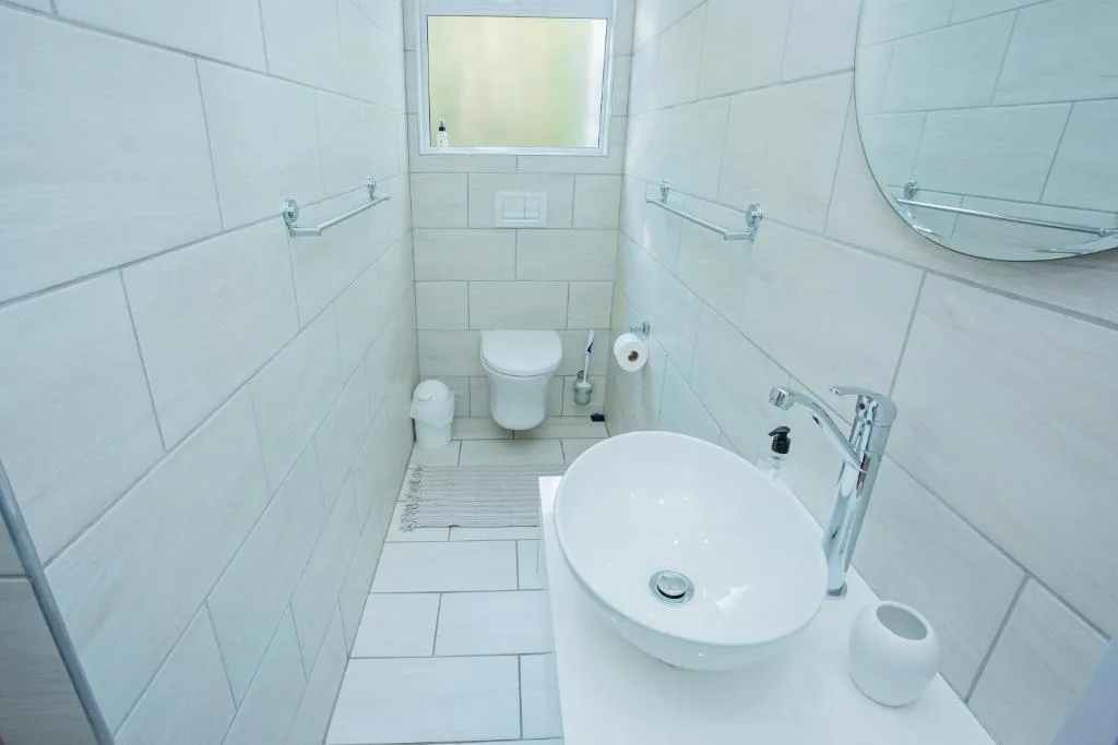 Clean white bathroom with round sink, toilet, and window