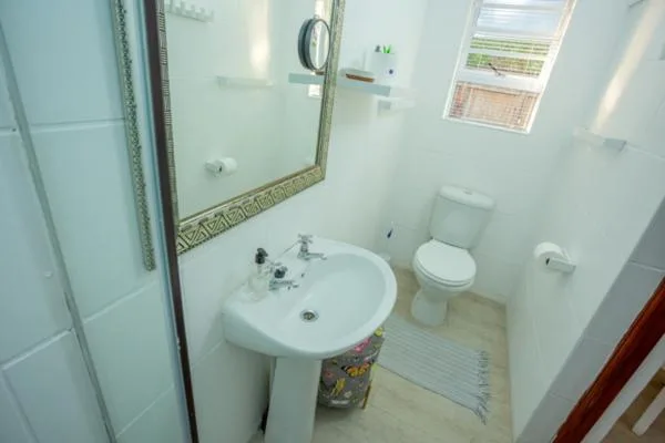 Clean bathroom with pedestal sink, toilet, and framed mirror
