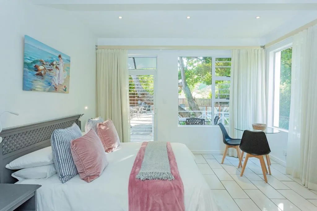 Bright bedroom with queen bed, pink accents, and glass doors opening to garden deck