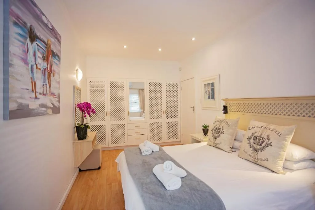 Bright modern bedroom with queen bed, decorative pillows, and white fitted wardrobes
