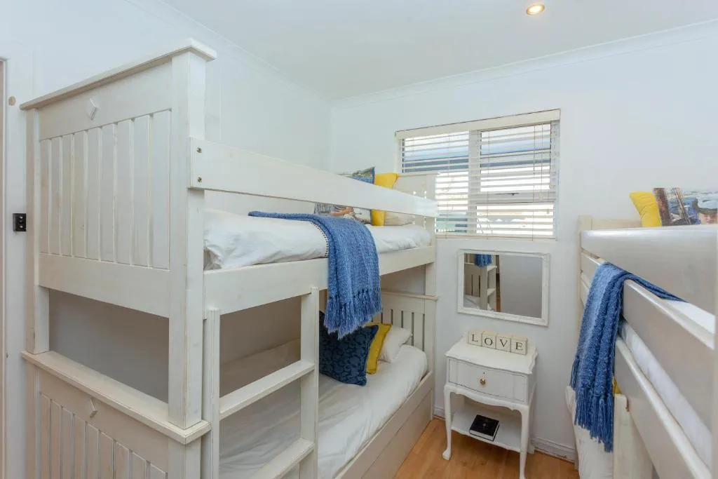 Bright bedroom with white bunk beds and blue accents, wooden floors