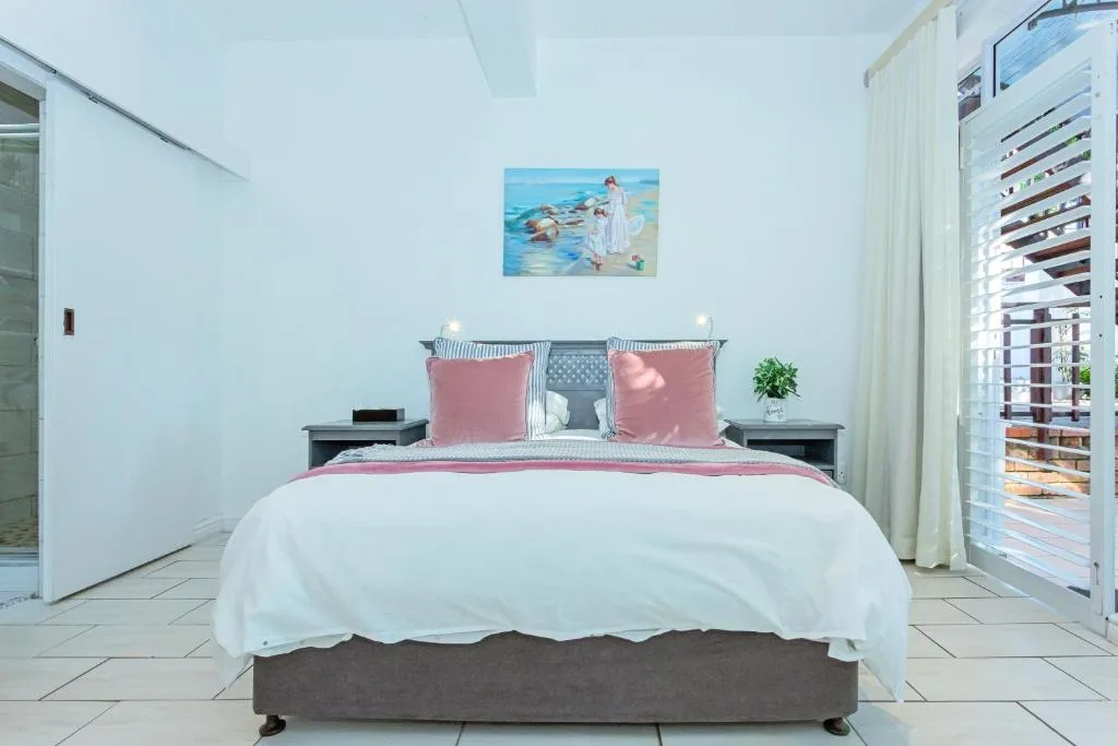 Bright bedroom with queen bed, pink accents, coastal artwork, and louvre doors