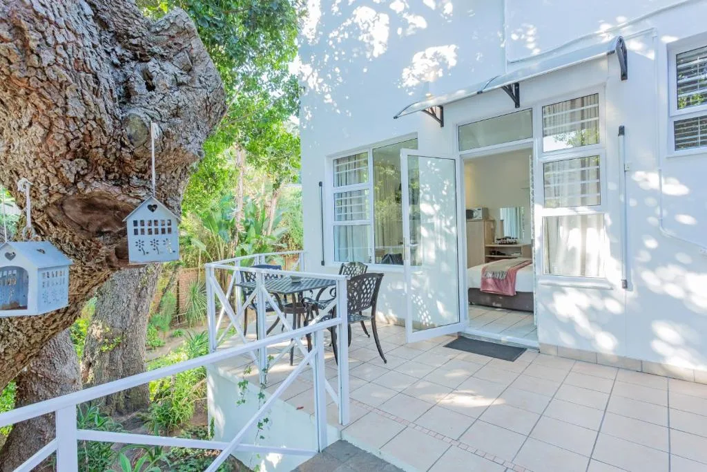 Patio area with dining chairs beside white cottage and mature tree