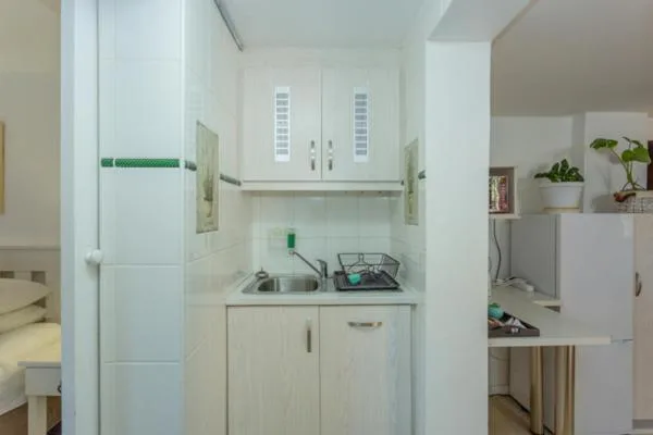Compact white kitchen with stove, sink, and refrigerator in apartment