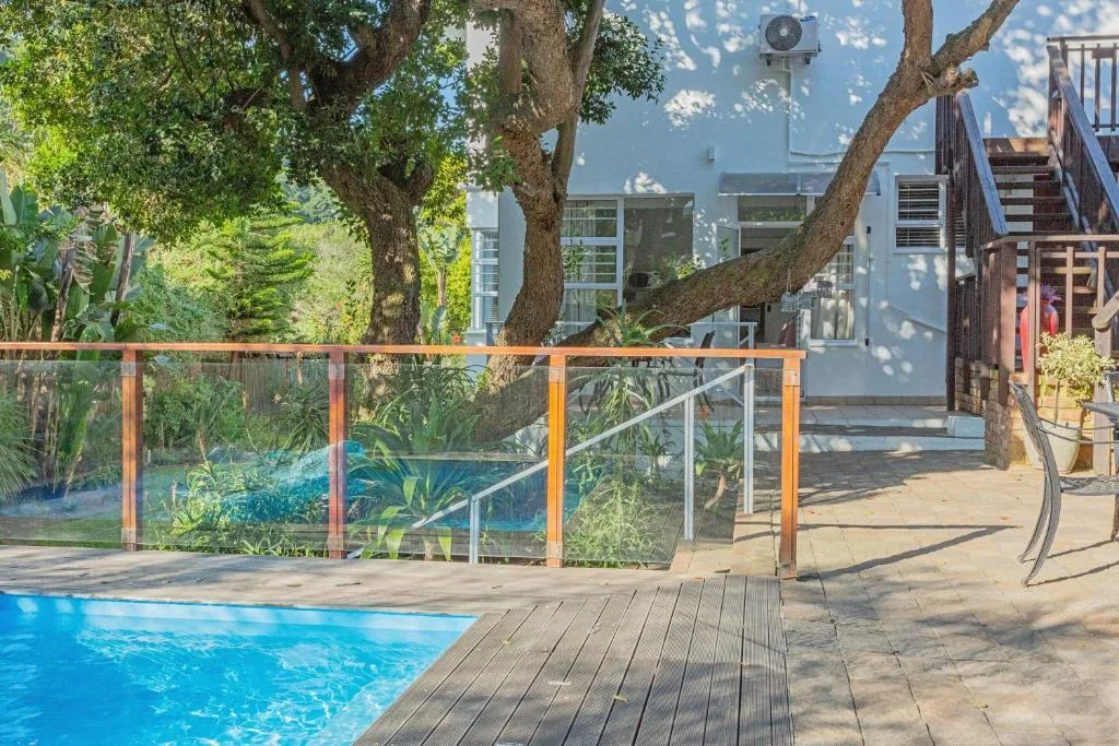 Swimming pool with wooden deck and glass safety fencing under mature trees