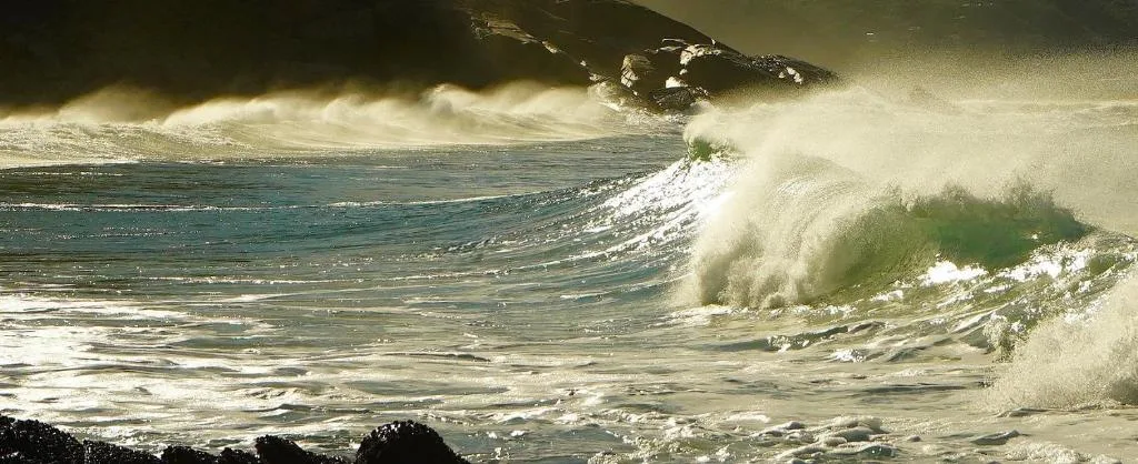 Dramatic ocean waves breaking on a sandy beach with rocky outcrops visible