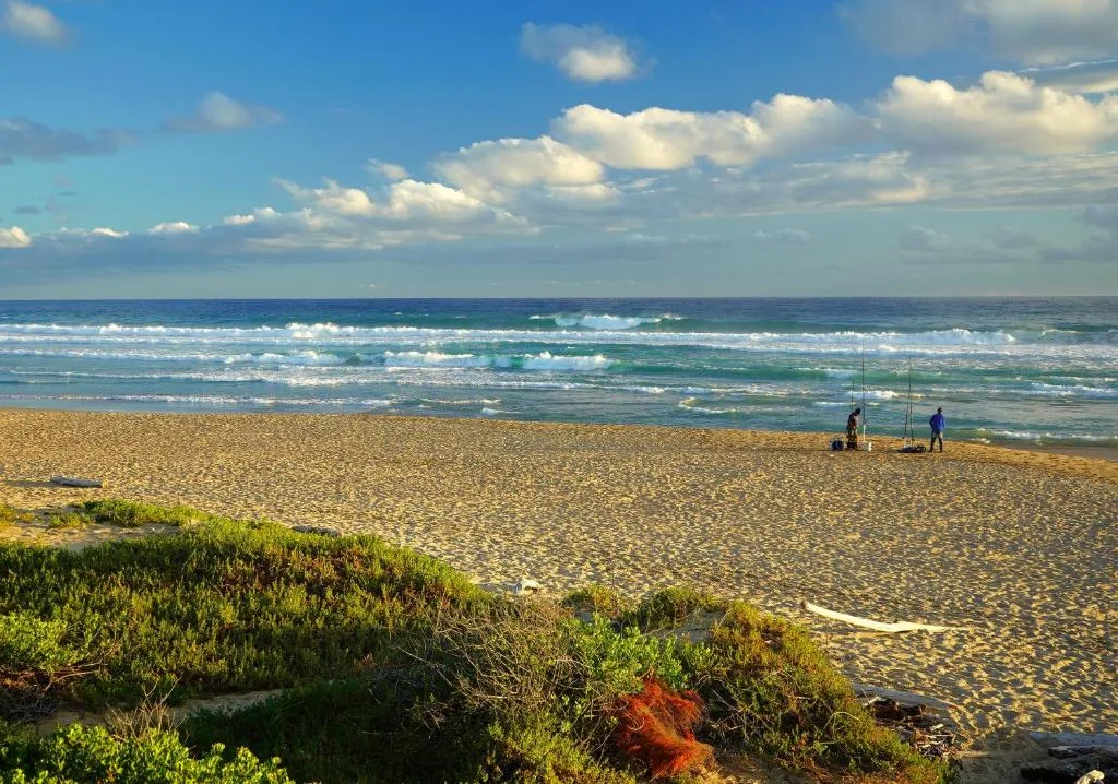 Pristine sandy beach with turquoise waves and cloudy blue sky overhead